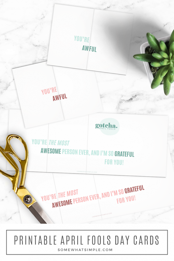 long image of some april fools day cards laying on the counter next to gold scissors and a green plant