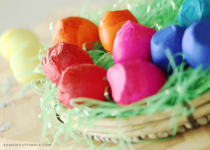 a shallow basket with green plastic Easter grass that is filled with red, pink, orange and blue cascarones