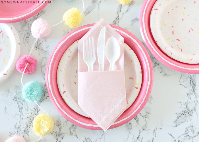 pink party place settings with plastic ware tucked inside a folded napkin pocket