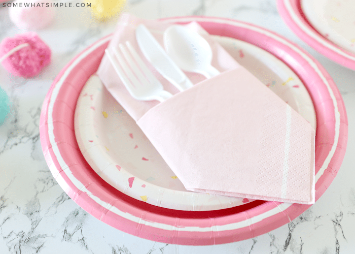 pink napkin pocket filled with white plasticware on a pink paper plate