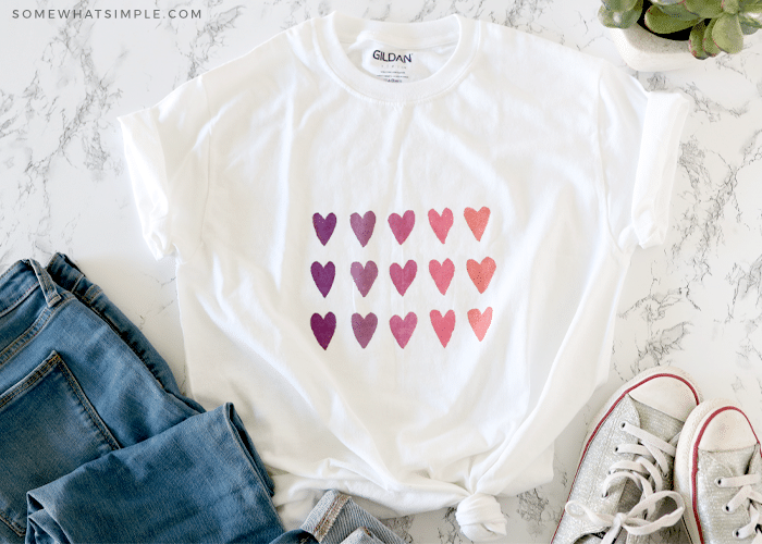 watercolor shirt with colorful hearts laying next to a pair of tennis shoes and jeans