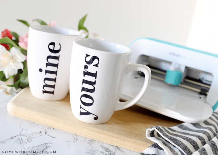 two white mugs colored with a sharpie. a cricut cutting machine in the background