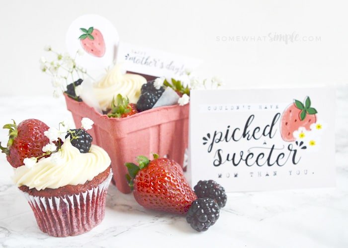 a red velvet cupcake topped with berries along with a small gift crate with another cupcake and berries sitting on the counter. Next to the gift is a Mother's Day card that reads couldn't have picked a sweeter mom than you