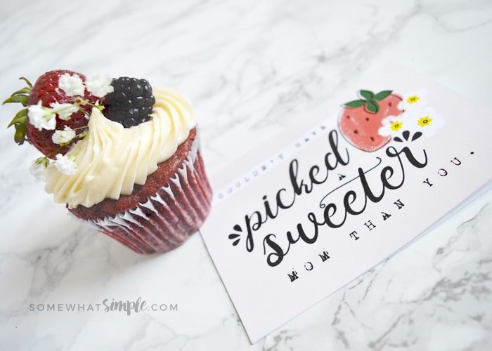 a cupcake topped with frosting and a strawberry and a blueberry next to a sweet mother's day card printable