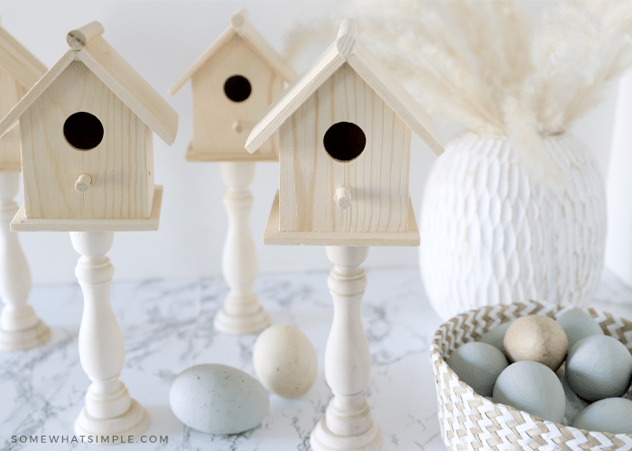 4 wood birdhouses on a white counter next to a basket of easter eggs